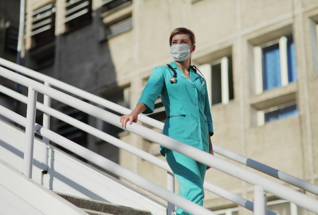 Médica ou enfermeira com uma máscara protetora subindo as escadas