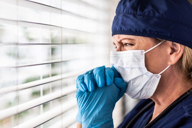 Foto médica ou enfermeira estressada em pausa na janela usando máscara médica