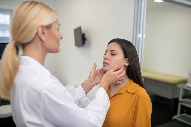 Médica palpitando os gânglios linfáticos da paciente em pé na frente dela