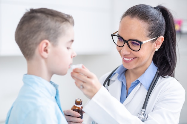 Foto médica pediatra que dá uma dose de xarope para tosse para um paciente jovem.