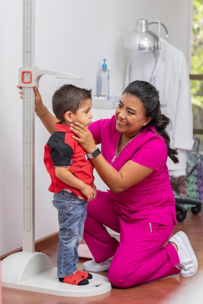 Médica pediatra que mide la altura de un niño con una regla de pedestal en su consultorio