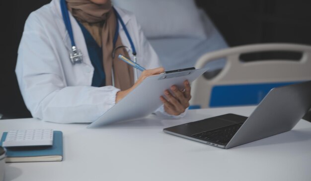 Una médica profesional y enfocada asiática en uniforme está trabajando y leyendo investigación médica en su portátil en su oficina en un hospital