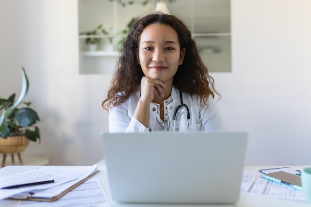 Médica profissional médica asiática vestindo uniforme fazendo anotações em diário médico preenchendo documentos histórico de doenças do paciente olhando para a tela do laptop estudante assistindo webinar