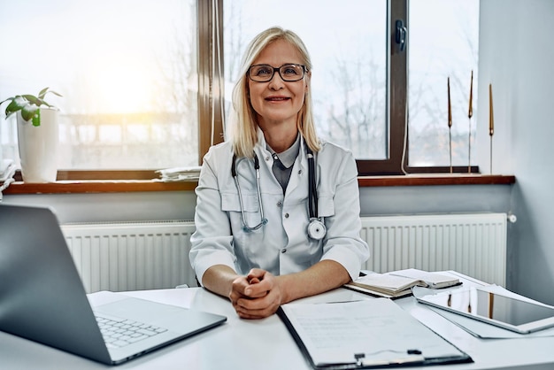 Médica que trabalha na mesa de escritório ela está sorrindo para os profissionais de saúde da câmera Vista frontal