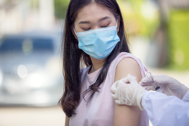 Médica segurando a seringa, tornando a dose de injeção de vacinação covid 19 no ombro de uma paciente usando máscara. F