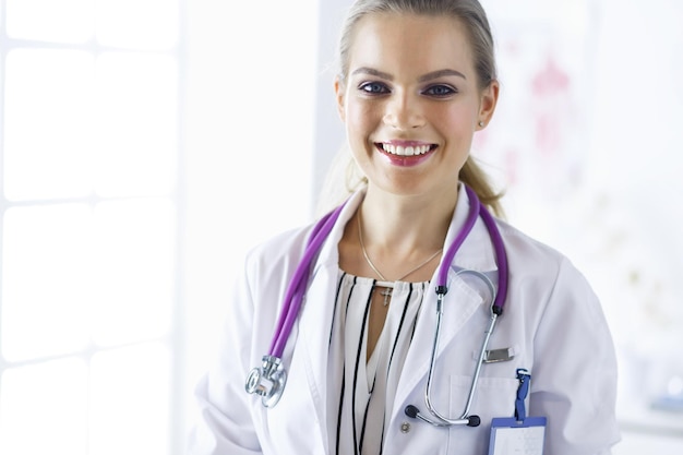 Médica sonriente con un estetoscopio médico de pie en uniforme