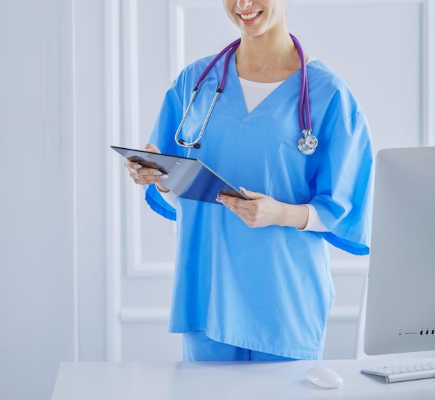 Médica sorridente com uma pasta em pé de uniforme