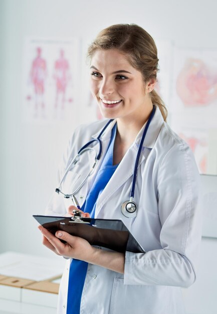 Médica sorridente com uma pasta em pé de uniforme