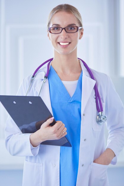 Médica sorridente com uma pasta em pé de uniforme