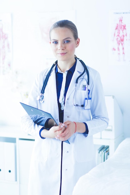 Médica sorridente com uma pasta em pé de uniforme