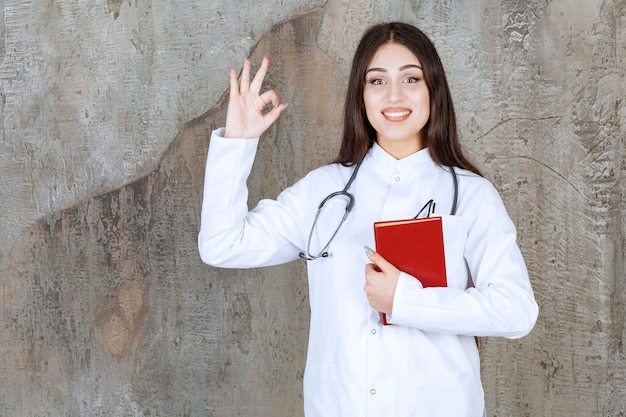 Médica sorridente fazendo um gesto de OK na parede cinza