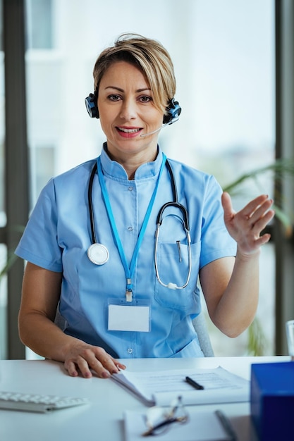 Médica sorridente usando fone de ouvido e se comunicando com um paciente enquanto trabalhava no call center médico