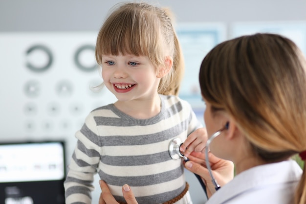 Foto médica trabalhando com uma linda garotinha sorridente em seu escritório