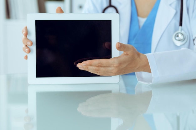 Médica usando computador tablet enquanto está sentado no local de trabalho, close-up das mãos. Conceito de medicina, saúde e ajuda.