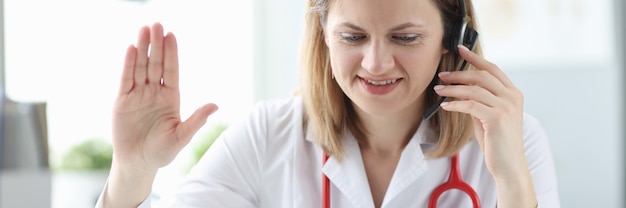 Médica usando fones de ouvido acenando com a mão para a tela do laptop