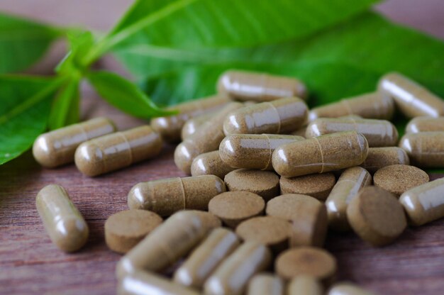 medicamento a base de hierbas en pastillas y cápsulas en una mesa de madera con hojas verdes