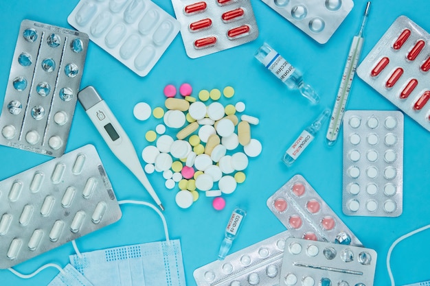 Medicamento para coronavírus. Medicamentos na luta contra o Covid-19. Comprimidos, seringas, termômetro, máscara médica sobre uma mesa azul. .