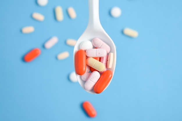 Medicamentos coloridos Pílulas em colher branca em fundo azul suplemento vitamínico colorido