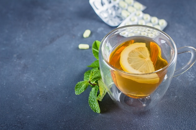 Medicamentos e saúde conceito de saúde. xícara de chá quente com limão, pílulas e termômetro