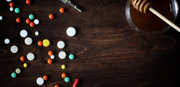 Medicamentos y pastillas en una mesa de madera. Varios medios para prevenir los resfriados. Té con limón y miel. Taza de vidrio con rodaja de limón y un tarro de miel.