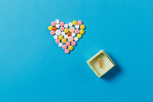 Medicamentos, tabletas redondas de colores blancos en forma de corazón aislado sobre fondo azul.