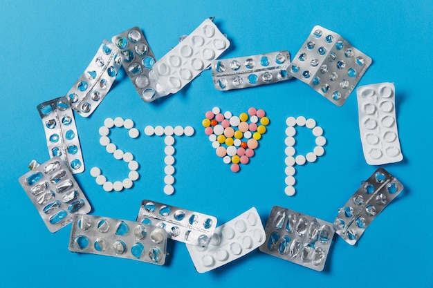 Medicamentos, tabletas redondas de colores blancos en Word Stop aislado sobre fondo azul.