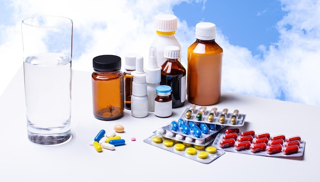 Medicamentos y un vaso de agua sobre una mesa blanca contra el cielo Medicamentos farmacéuticos en contenedores Tabletas capsulares temáticas de farmacia con antibiótico medicinal en paquetes