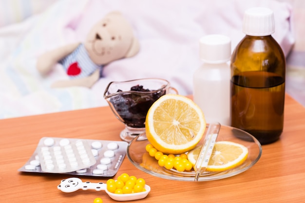 Medicamentos, vitaminas, limón y mermelada en la mesa cama infantil con un peluche