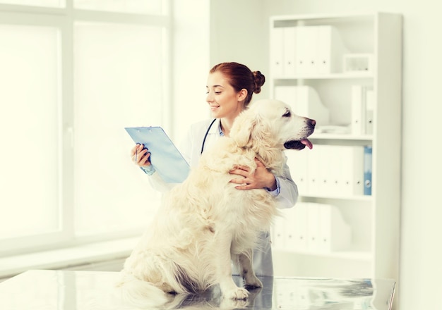 Medicina, animal de estimação, animais, cuidados de saúde e conceito de pessoas - feliz veterinário ou médico com cachorro golden retriever e prancheta na clínica veterinária