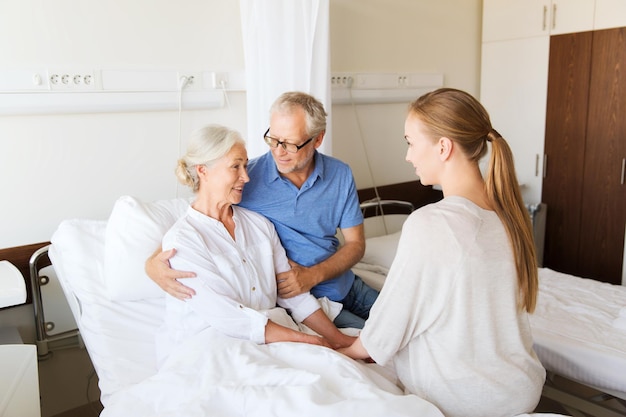 medicina, apoio, cuidados de saúde da família e conceito de pessoas - feliz homem sênior e jovem visitando e torcendo sua avó deitada na cama na enfermaria do hospital