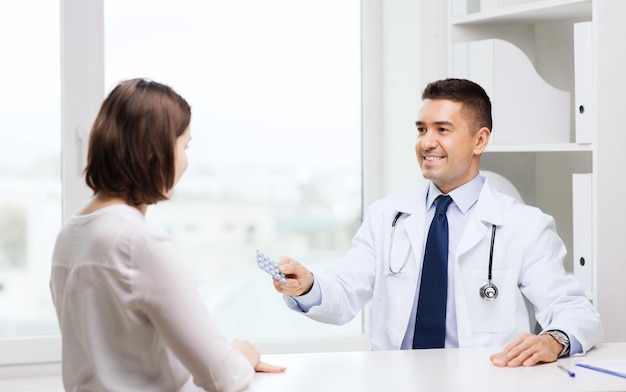 medicina, atención de la salud, medicación y concepto de personas - médico sonriente con portapapeles que da pastillas a una mujer joven en el hospital