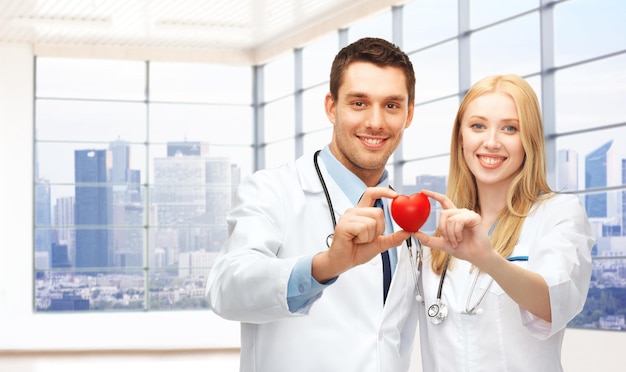 medicina, cardiologia, saúde e conceito de pessoas - cardiologistas de jovens médicos felizes com coração vermelho sobre fundo clínico