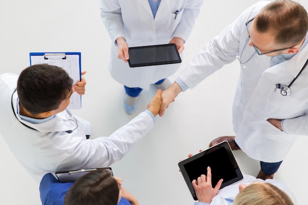 Foto medicina, cuidados de saúde e conceito de gesto - grupo de médicos com computadores tablet cumprimentando-se com um aperto de mão no hospital