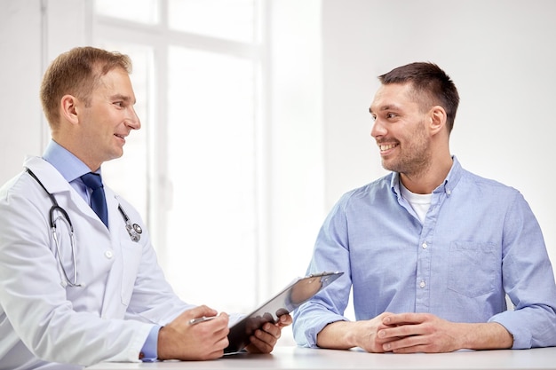 medicina, cuidados de saúde, pessoas e conceito de câncer de próstata - feliz médico masculino com prancheta e reunião de pacientes e conversando no hospital