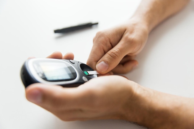 medicina, diabetes, glicemia, cuidados de saúde e conceito de pessoas - close-up do homem verificando o nível de açúcar no sangue com glicosímetro e faixa de teste em casa