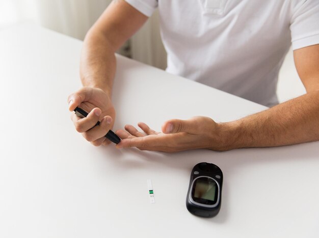 Medicina, diabetes, glucemia, atención de la salud y concepto de personas: cierre del hombre que controla el nivel de azúcar en la sangre con glucómetro en casa