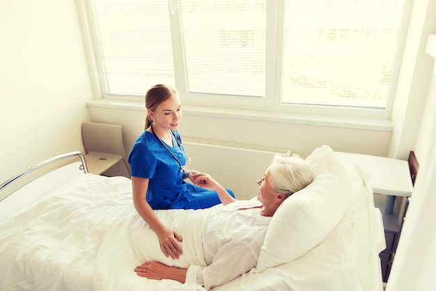 Foto medicina, edad, apoyo, atención médica y concepto de personas - médico o enfermera visitando y animando a una anciana acostada en la sala del hospital