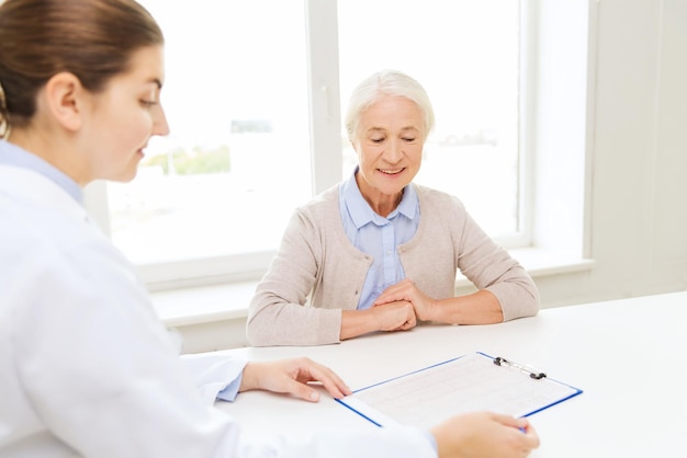 medicina, edad, atención de la salud y concepto de personas - médico con portapapeles y reunión de ancianas en el hospital