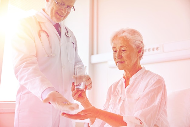 medicina, edad, atención de la salud y concepto de personas: médico que da medicamentos y agua a una anciana en la sala del hospital