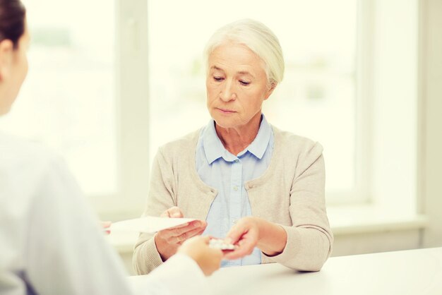 Medicina, edad, atención de la salud y concepto de personas: médico que da recetas y pastillas a una anciana en el hospital