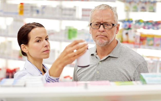 medicina, farmacêutica, cuidados de saúde e conceito de pessoas - farmacêutico mostrando droga para cliente sênior na farmácia