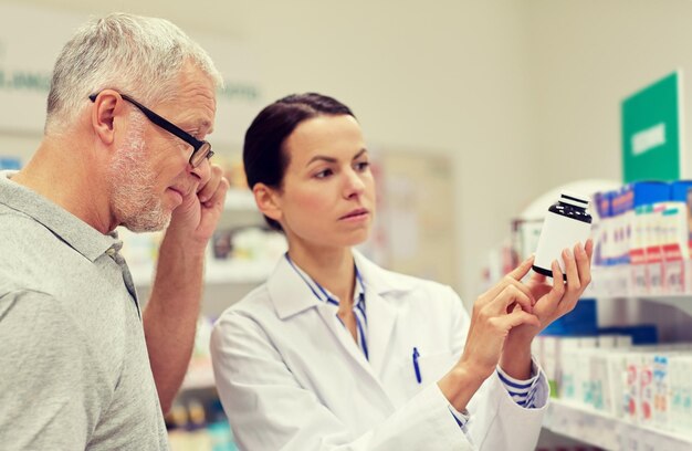 medicina, farmacêutica, cuidados de saúde e conceito de pessoas - farmacêutico mostrando droga para cliente sênior na farmácia