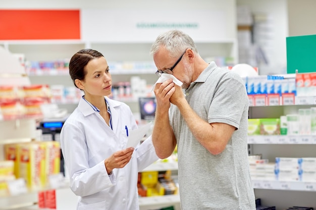 Medicina, farmacia, atención de la salud y concepto de personas: farmacéutico y anciano enfermo con gripe que sopla la nariz en la farmacia