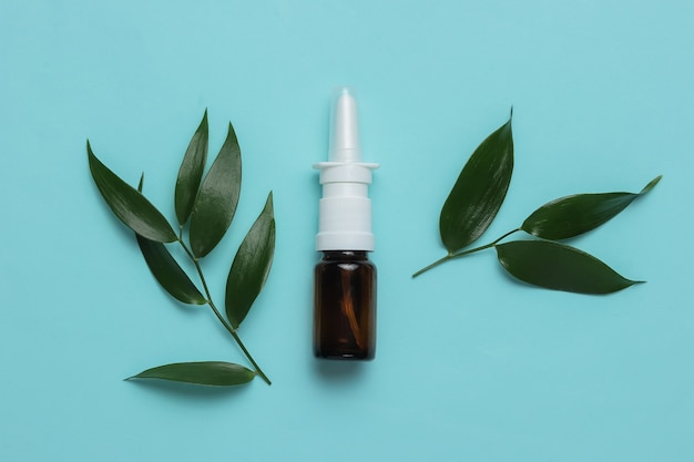 Medicina herbaria pastillas blancas spray nasal con hojas verdes sobre fondo azul.