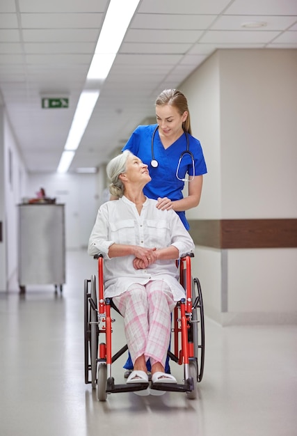 medicina, idade, apoio, cuidados de saúde e conceito de pessoas - enfermeira feliz levando paciente sênior em cadeira de rodas no corredor do hospital