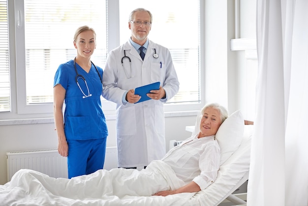 medicina, idade, cuidados de saúde e conceito de pessoas - médico e enfermeiro com computador tablet pc visitando mulher paciente sênior na enfermaria do hospital