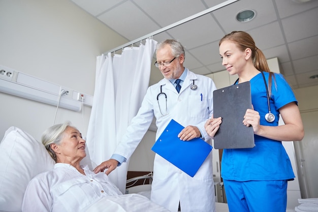 medicina, idade, cuidados de saúde e conceito de pessoas - médico e enfermeiro com pranchetas visitando paciente sênior na enfermaria do hospital