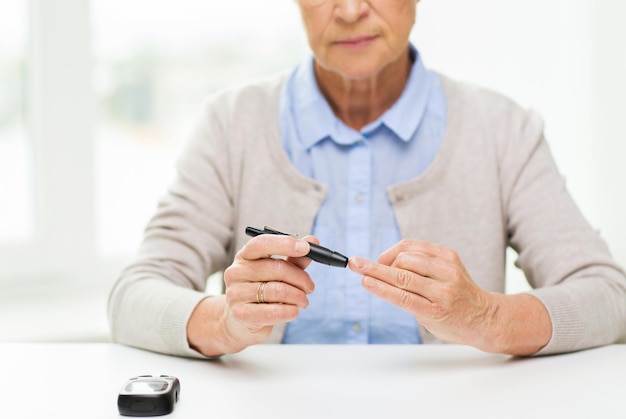 medicina, idade, diabetes, cuidados de saúde e conceito de pessoas - close-up de mulher sênior com glicosímetro, verificando o nível de açúcar no sangue em casa