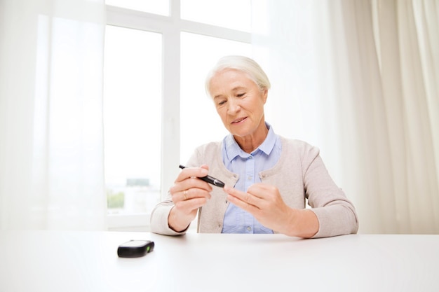 medicina, idade, diabetes, cuidados de saúde e conceito de pessoas - mulher sênior feliz com glicosímetro verificando o nível de açúcar no sangue em casa