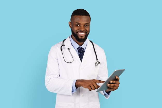 Medicina moderna sorrindo jovem médico negro de uniforme posando com tablet digital